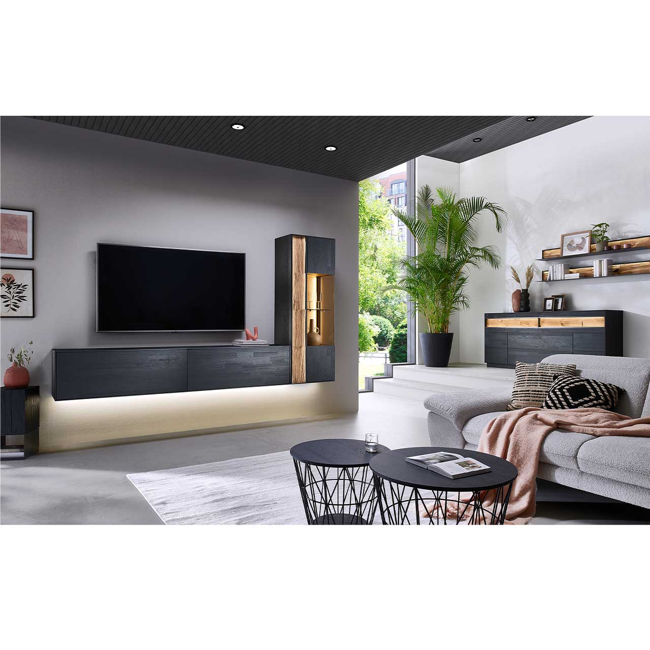 Modernes Wohnzimmer mit dreiteiliger Wohnwand aus massiver Kernesche anthrazit: Hängelowboard und zwei Wandregale. Links das passende Sideboard mit Wandpaneelen. Im Vordergrund zwei dazugehörige Couchtische. 