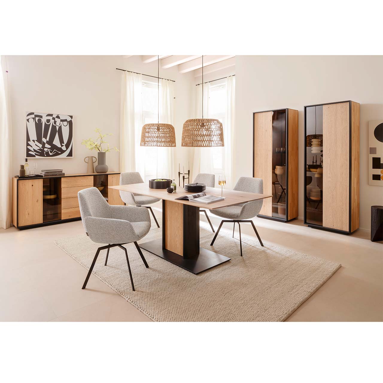 Modern eingerichtetes Esszimmer mit Massivholzmöbeln aus Kerneiche Natur mit einem rechteckigen Holztisch und vier hellen Stühlen. Links an der Wand ein Sideboard mit Glasausschnitt, rechts zwei Standvitrinen jeweils mit einer Holz-/Glastür.