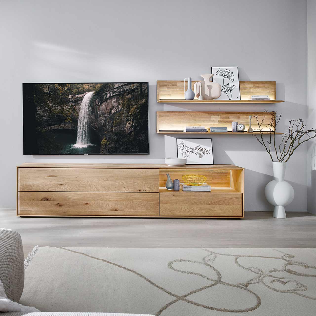 Moderne dreiteilige Wohnwand aus massiver Kerneiche Natur bestehend aus einem Lowboard mit Schubkästen und beleuchteter Nische sowie zwei beleuchteten Wandpaneelen mit Holzboden und geschroppter Rückwand.