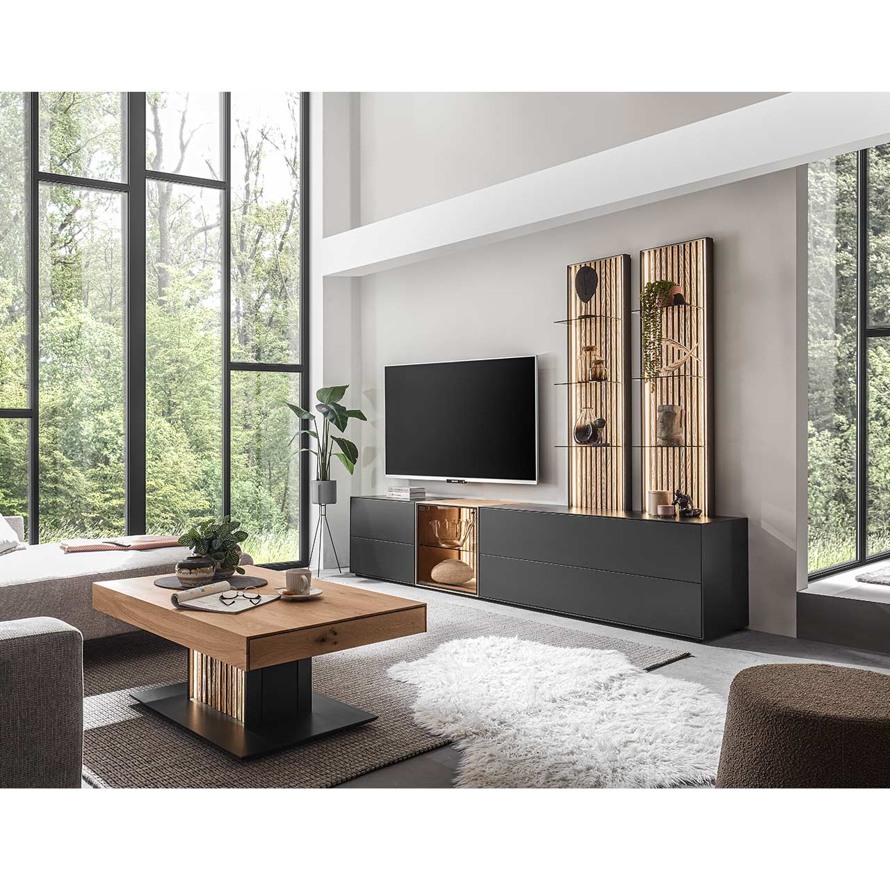 Modern eingerichtetes Wohnzimmer mit fünfteiliger Wohnwand bestehend aus Lowborads in anthrazit mit Glastüren und Wandpaneelen in hellem Holz mit Lamellen. Davor der passende helle Couchtisch.