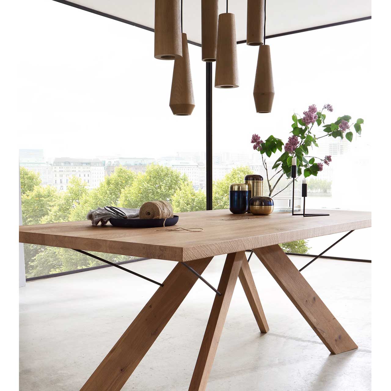 Bildausschnitt eines Esszimmertisches aus massivem Holz mit sternförmigem Holzgestell, darüber hängend sechs unterschiedliche geometrische Holzkörper als Pendelleuchte.