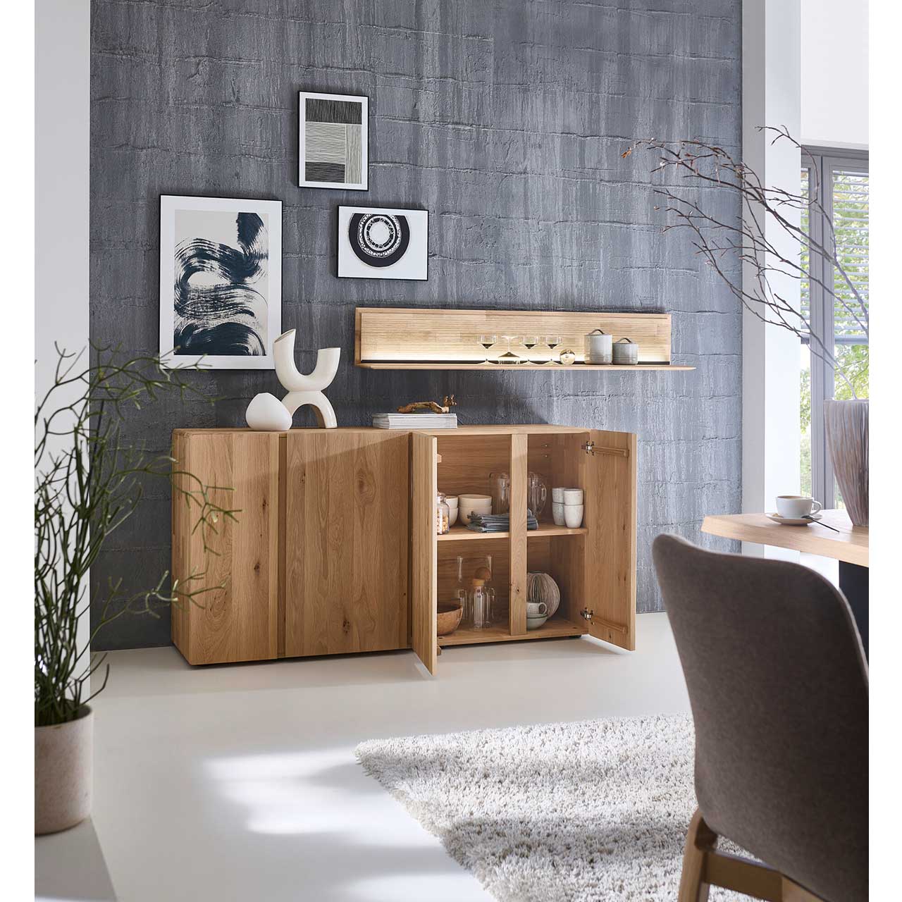 Modernes Sideboard aus massivem Eichenholz mit vier Türen. Die beiden rechten Türen sind geöffnet und zeigen innenliegenden zwei Holzeinlegeböden. Über dem Sideboard hängt ein langes, beleuchtetes Wandboard.