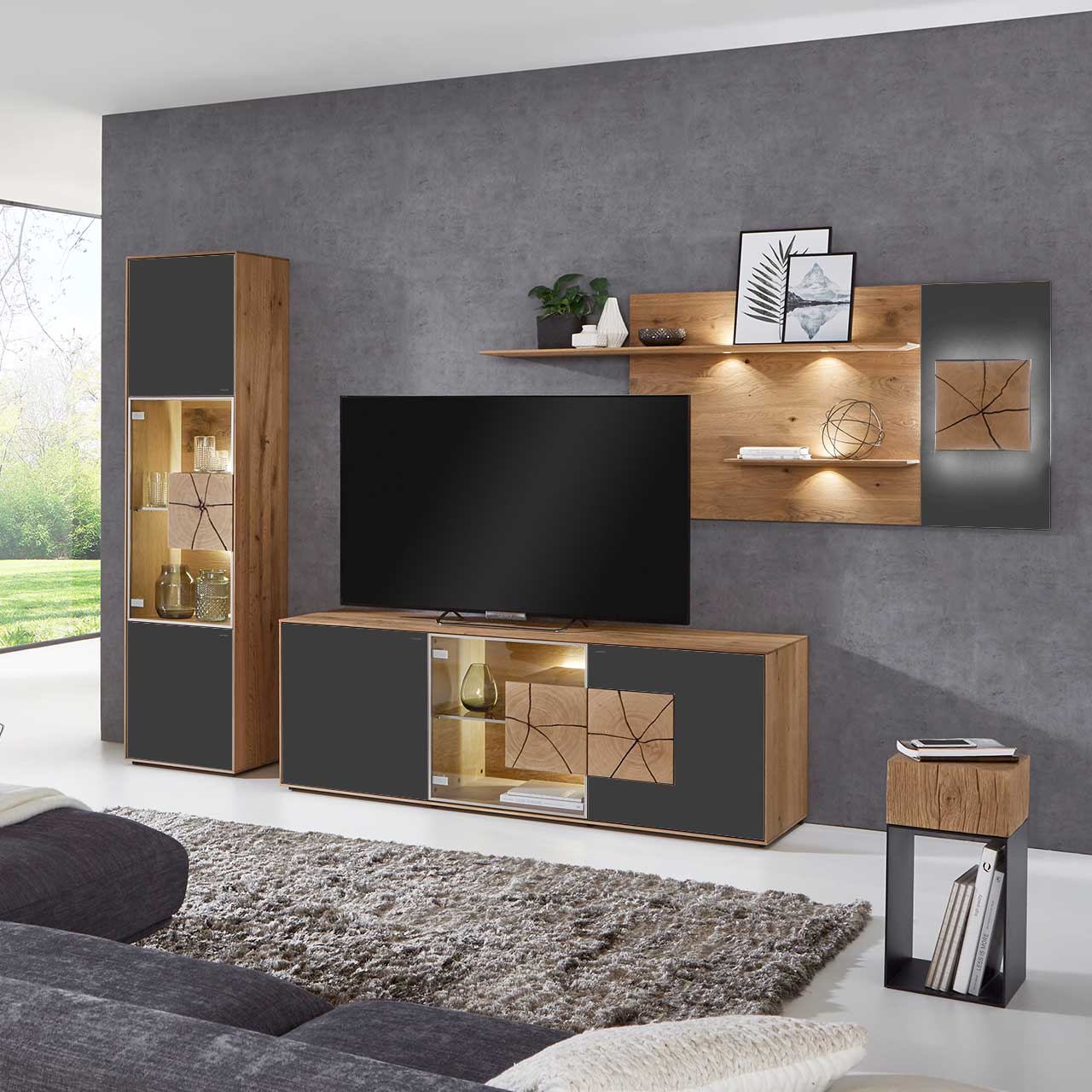 Wohnzimmer mit moderner dreiteiliger Massivholz Wohnwand mit Mattglas Anthrazit Fronten und Hirnholzscheiben: Lowboard mit Glastür und beleuchtetem Hirnholzblock, Wandpaneel mit Regalböden, Standvitrine mit beleuchtetem Glasausschnitt und Hirnholz.