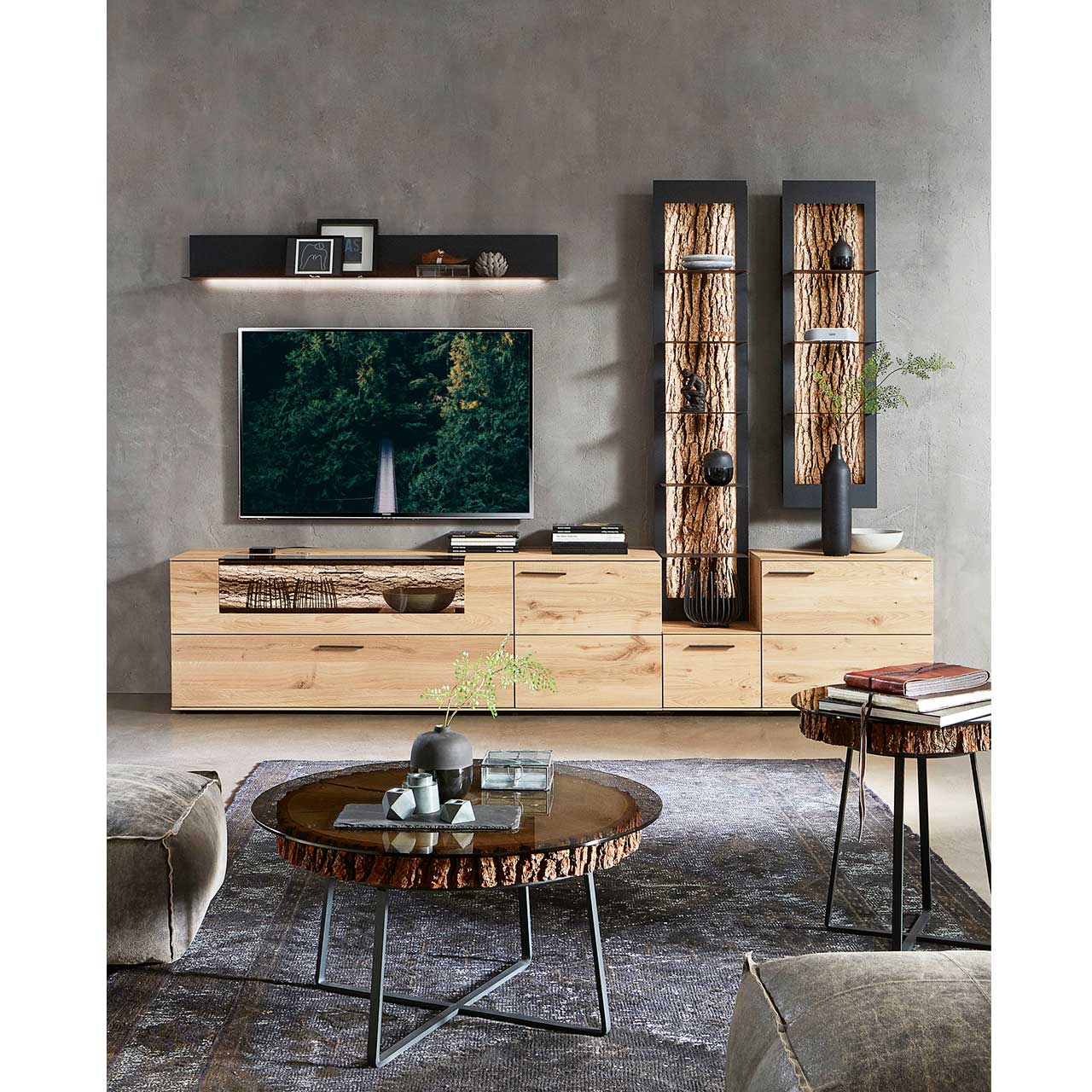 Milieubild Wohnzimmer - Hartmann NATURWERKE - Beistelltische 8400C-0472 und 0473 Wohnzimmer mit moderner Massivholz Wohnwand: Lowboard, Wandpaneel und zwei Wandregale. Im Vordergrund ein kleiner und ein großer Beistelltisch mit runder Glasplatte auf echter Baumscheibe und filigranem Metallgestell in Anthrazit.