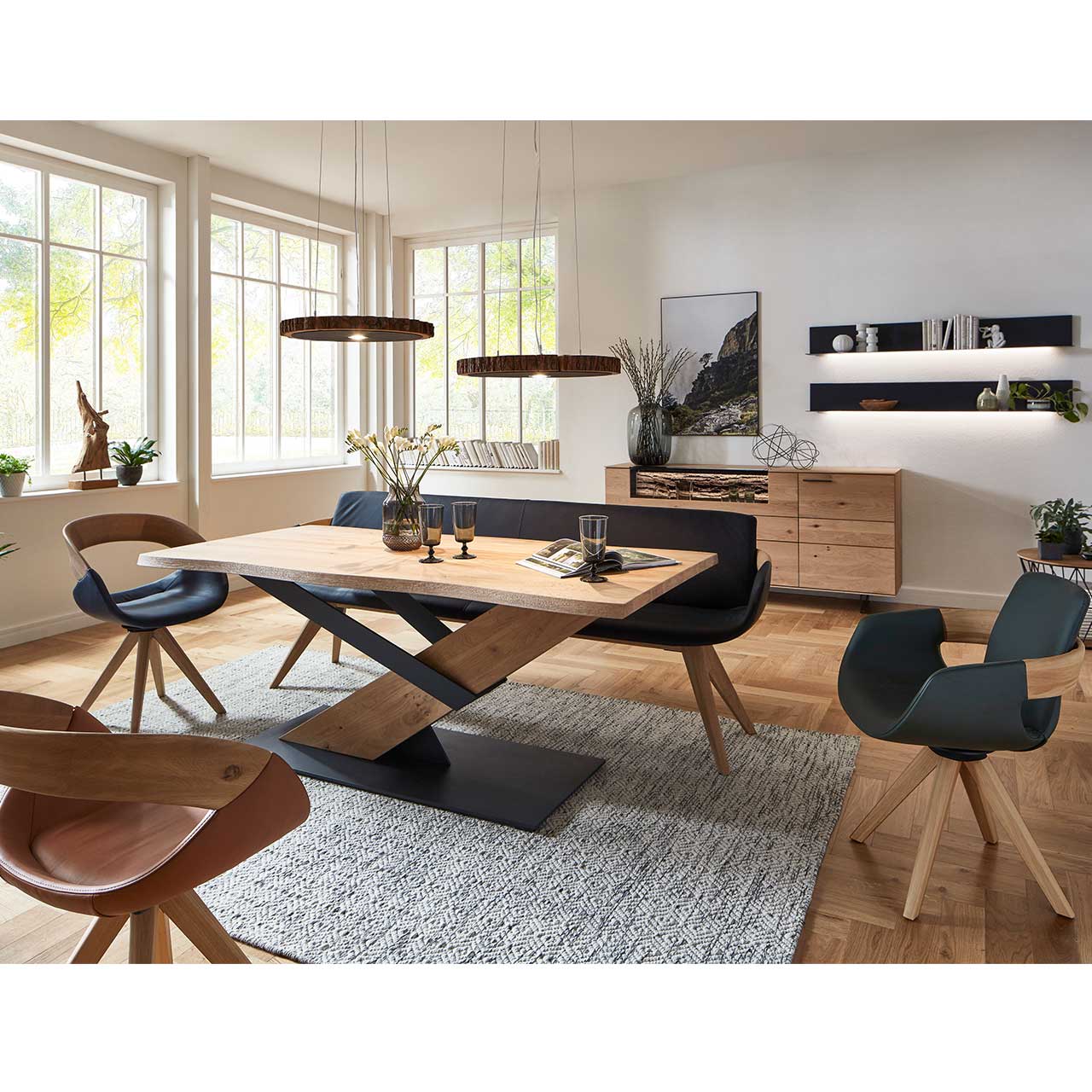 Modernes Esszimmer mit massivem Holztisch, drei Drehstühlen auf Holzgestell und einer Sitzbank in schwarzem Leder. Über dem Tisch hängen zwei Tellerleuchten aus echter Holzscheibe. Dahinter an der Wand das passende Sideboard und zwei Wandpaneele.