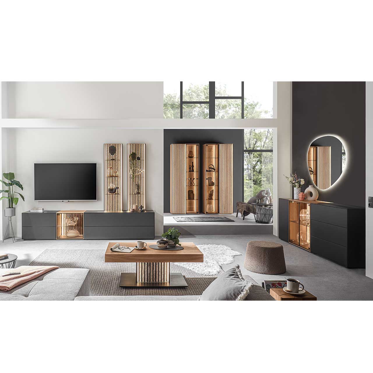Modern eingerichtetes Wohnzimmer mit fünfteiliger Wohnwand in Anthrazit kombiniert mit hellem Holz und Lamellen. Rechts das passendem Sideboard mit Glasfront. Im Vordergrund heller Couchtisch, im Hintergrund zwei helle Standvitrinen mit Lamellen.