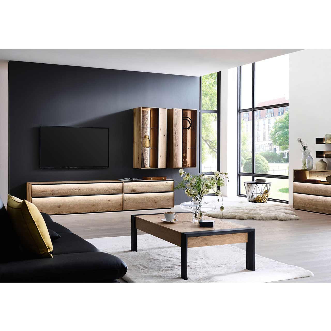 Wohnzimmer Milieubild mit Massivholzwohnwand aus Lowboard und 2 Hängevitrinen vor dunkler Wand