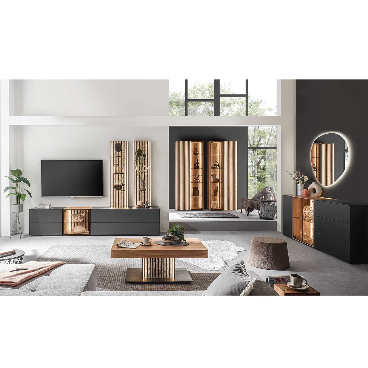Modern eingerichtetes Wohnzimmer mit fünfteiliger Wohnwand in Anthrazit kombiniert mit hellem Holz und Lamellen. Rechts das passendem Highboard. Im Vordergrund heller Couchtisch, im Hintergrund zwei helle Standvitrinen mit Lamellen.