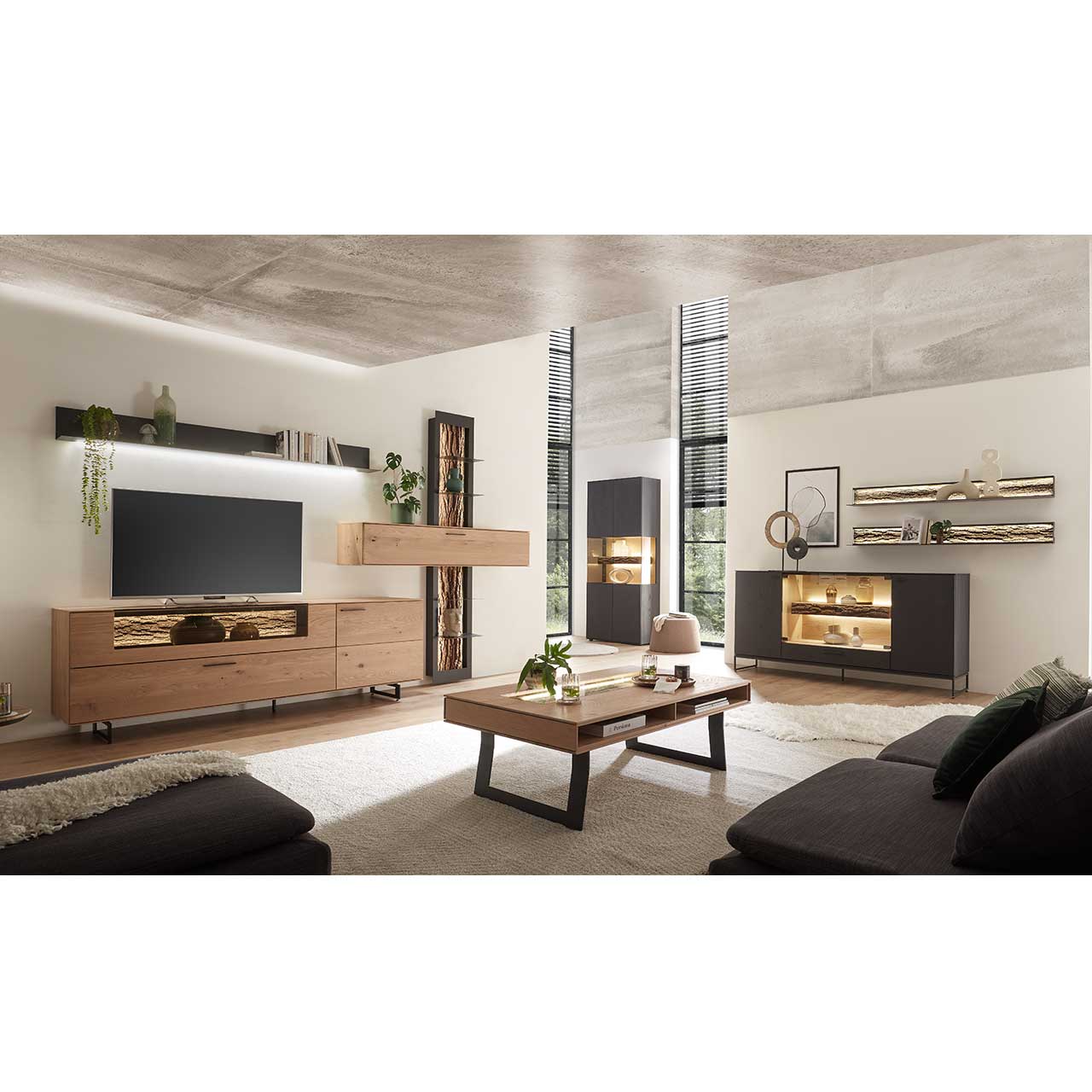 Modernes Wohnzimmer mit Wohnwand aus Kerneiche Natur und einem Sideboard mit edler anthrazit Beizung, mit beleuchteten Glasausschnitt und Rinden-Akzent. Darüber zwei moderne Wandregale.