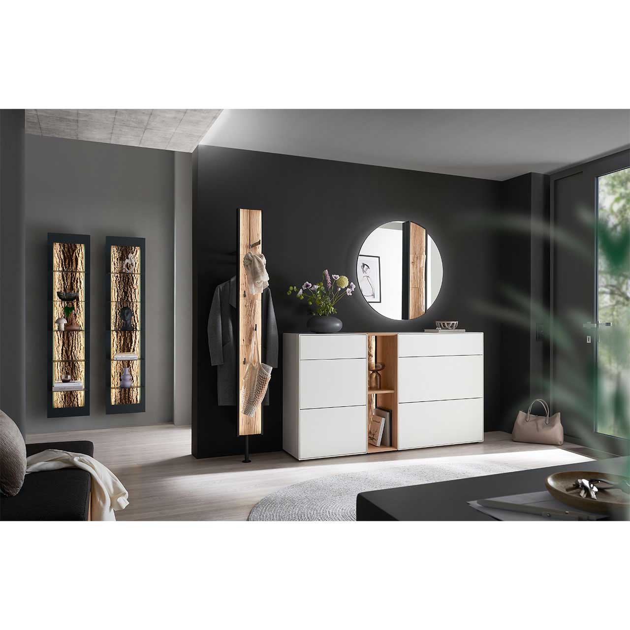Milieubild Hartmann SALVO Garderoben - Wandspiegel 8550G-5096 re. - mit Spaltholz Flur mit modernen Garderobenmöbeln aus Kernbirke und Kerneiche Natur: Regalelement mit Spaltholz-Rückwand zwischen zwei weiß lackierten Stauraumschränken, dazu ein Garderobenpaneel und ein runder Spiegel mit Spaltholz-Akzent.