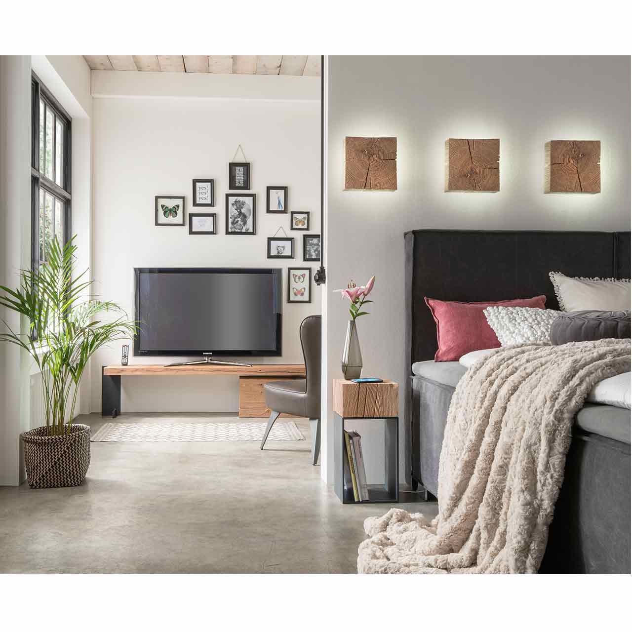 Eingerichtetes Schlafzimmer mit Bett, darüber drei quadratische Wandlampen aus massivem Holzblock, links daneben der passende Beistelltisch mit Holzkorpus und Untergestell Metall Anthrazit.