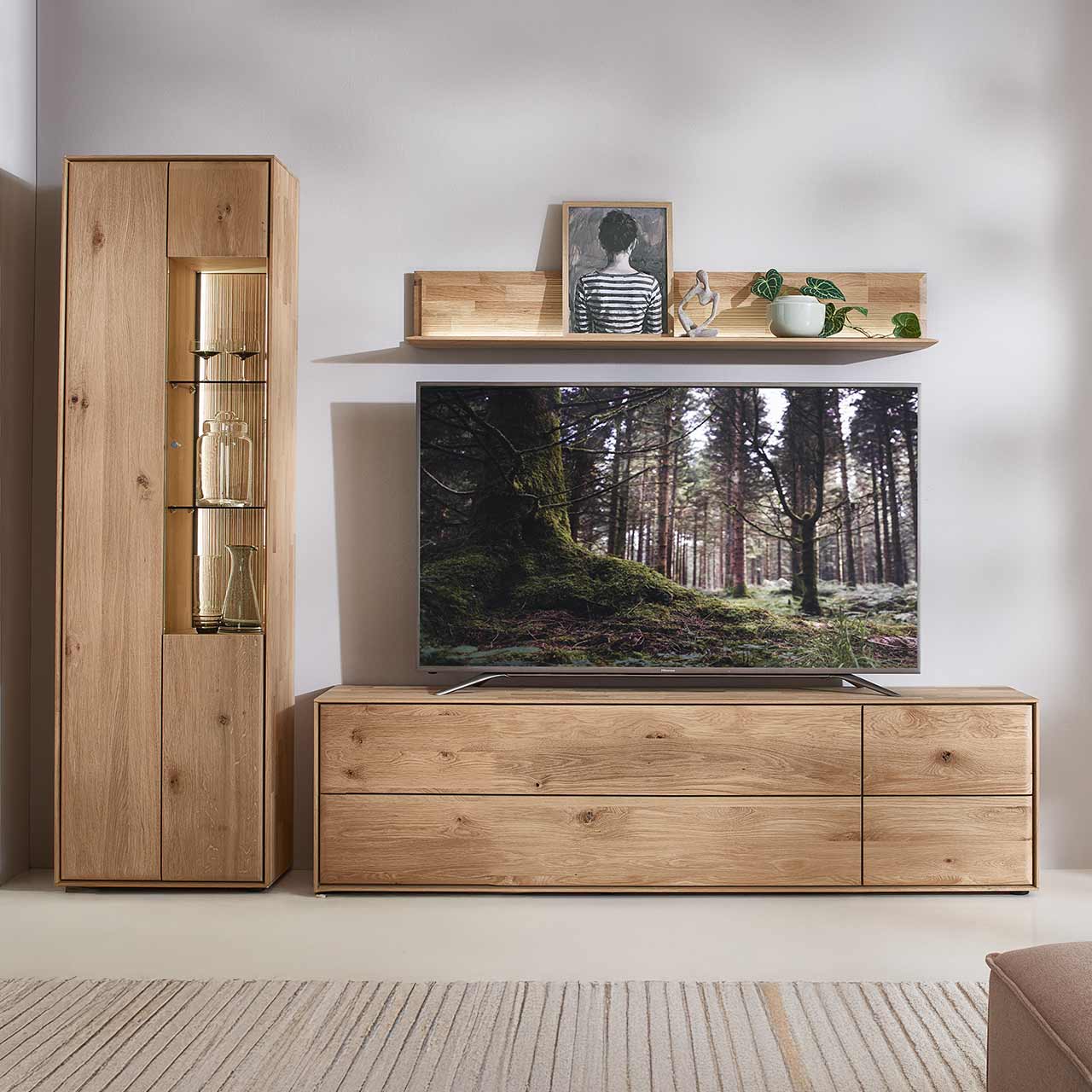 Hartmann VALA - Wohnkombination 8640 Nr. V40 - dreiteilig Moderne dreiteilige Wohnwand aus massiver Kerneiche Natur bestehend aus einer beleuchteten Standvitrine mit zwei Türen, einem breitem Wandregal mit Holzboden und geschroppter Rückwand und einem Lowboard mit Klappe, Tür und Schubkasten.
