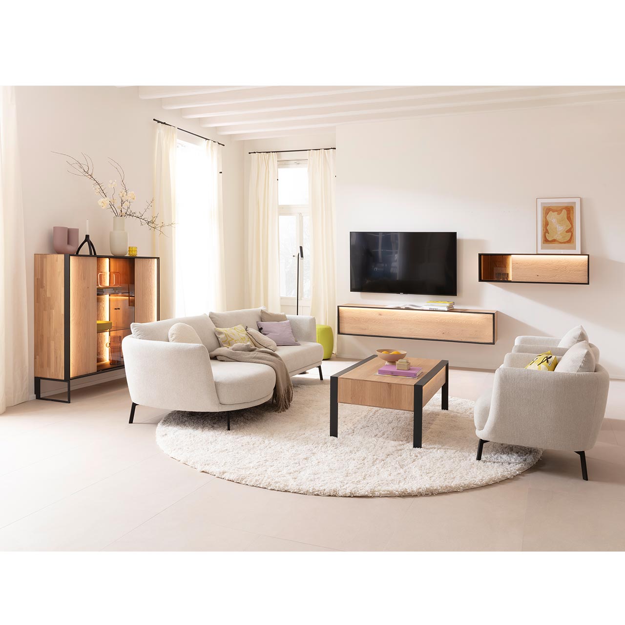 Eingerichtetes Wohnzimmer mit Massivholzmöbeln aus heller Kerneiche Natur: Highboard auf Metallkufen anthrazit mit beleuchteter Front und Glastüren, schlichtes Hängelowboard, Hängeschrank mit Glasausschnitt und passender Holz-Couchtisch auf Metallfüßen. 