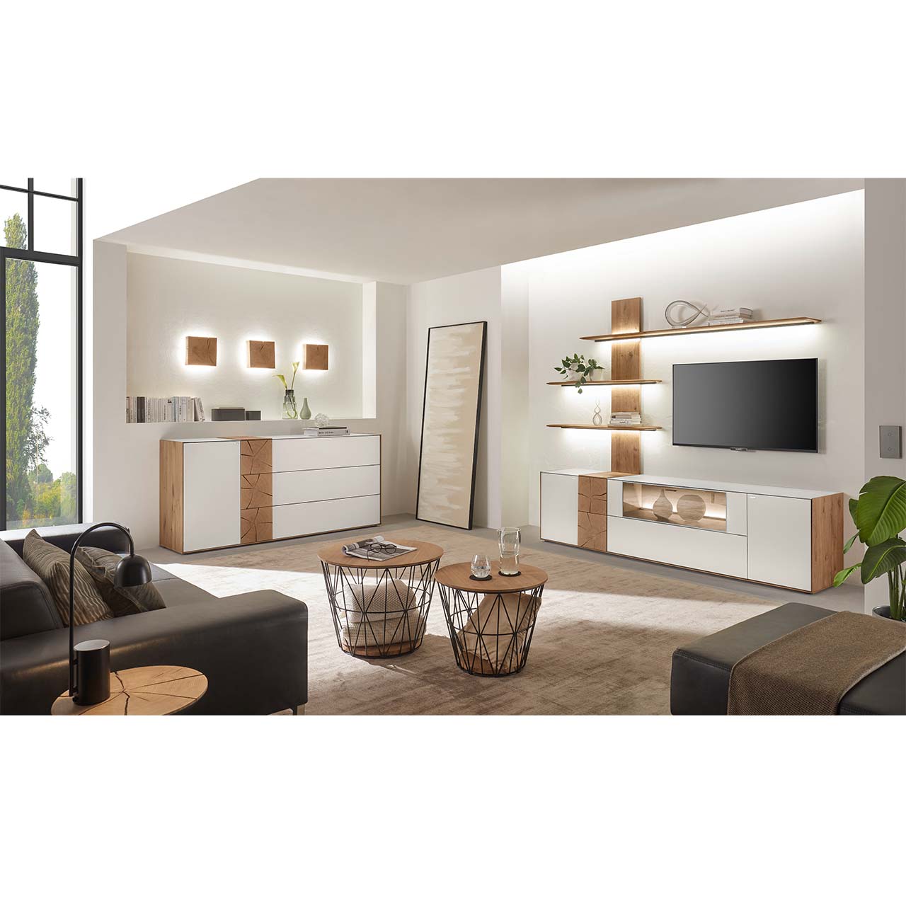 Wohnzimmer mit TV und moderner Wohnwand aus massiver Kerneiche mit Hirnholz und Mattglas weiß Fronten, mit Lowboard und Wandpaneel mit Regalböden. Links das passende Sideboard, darüber drei Holzwand-Leuchten. Im Vordergrund zwei runde Couchtische.