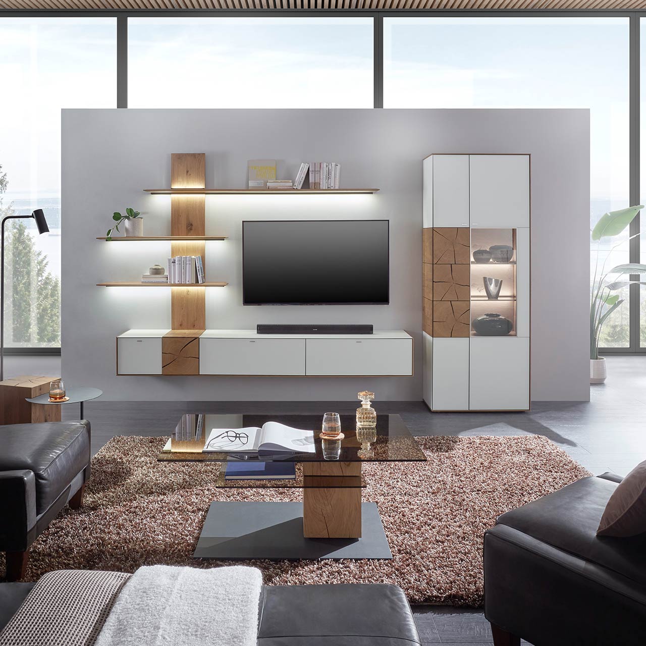 Moderne Wohnwand aus massiver Kerneiche mit Mattglas weißen Fronten, mit Hängelowboard, Wandpaneel mit Regalböden und Standvitrine. Im Vordergrund der passende Couchtisch mit rechteckiger Glasplatte.