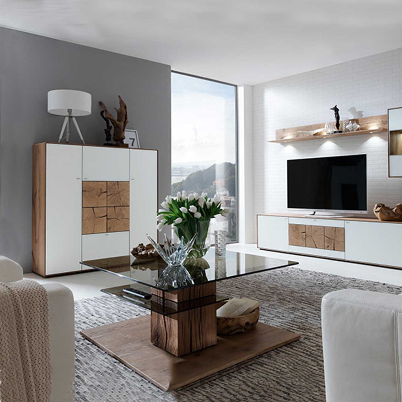 Modernes Highboard aus massiver Kerneiche Umato mit Mattglas weiß Fronten und vier dekorativen, rechteckigen Hirnholzscheiben in heller Kerneiche Umato mittig platziert - in einem Wohnzimmer stehend, davor passender Glas-Couchtisch.