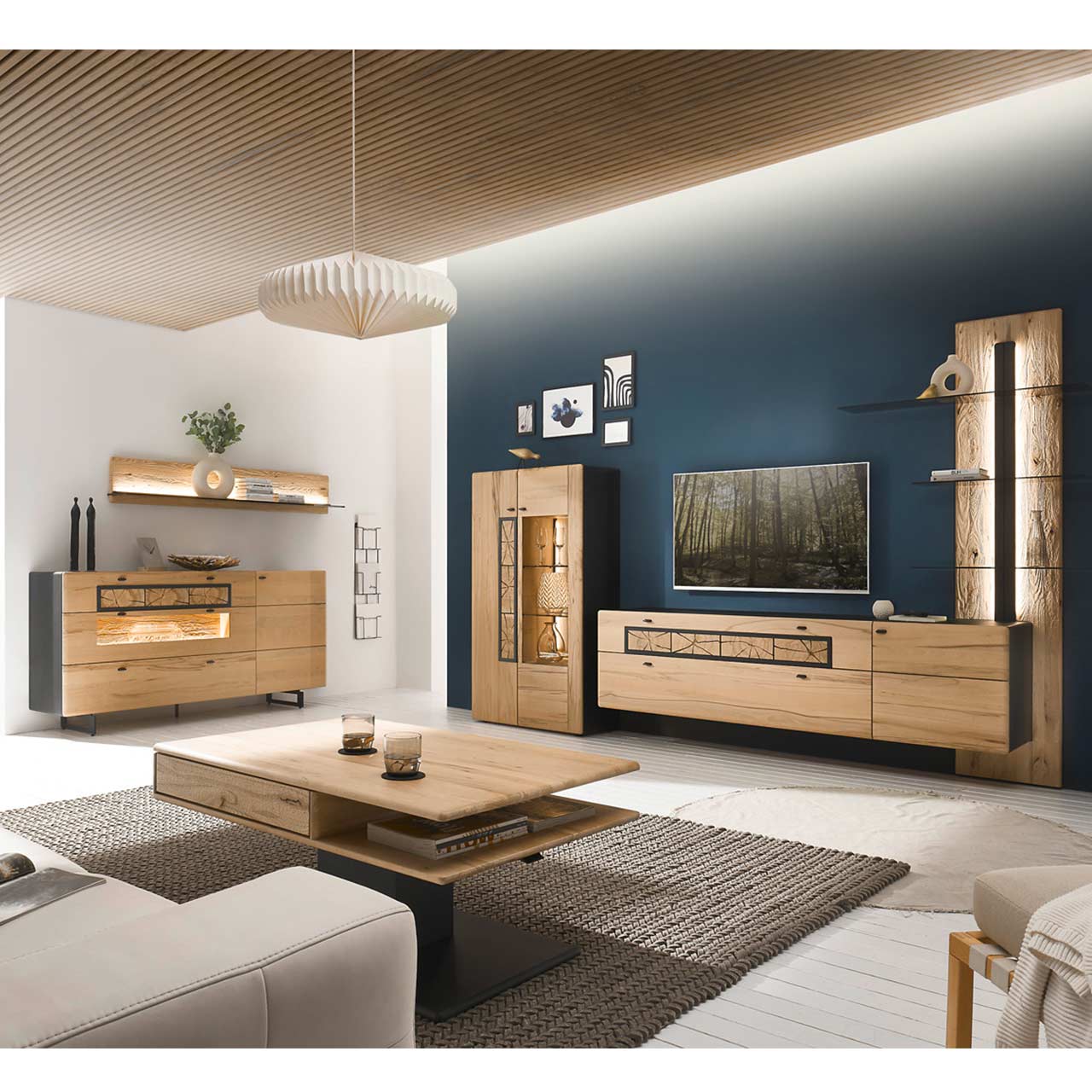 Eingerichtetes Wohnzimmer mit moderner Wohnwand aus Kernbuche vor einer dunkelblauen Wand bestehend aus Highboard, Lowboard und Paneel. Rechts das passende Sideboard auf Metallkufen darüber ein Regal. Im Vordergrund der dazugehörige Couchtisch.