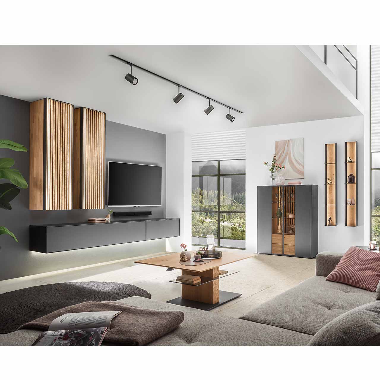 Modernes Wohnzimmer mit Wohnwand aus massivem Holz anthrazit lackiert und hellen Holzlamellen. Rechts an der Wand das passende Highboard und zwei Wandregale. Im Vordergrund der dazugehörige Couchtisch.
