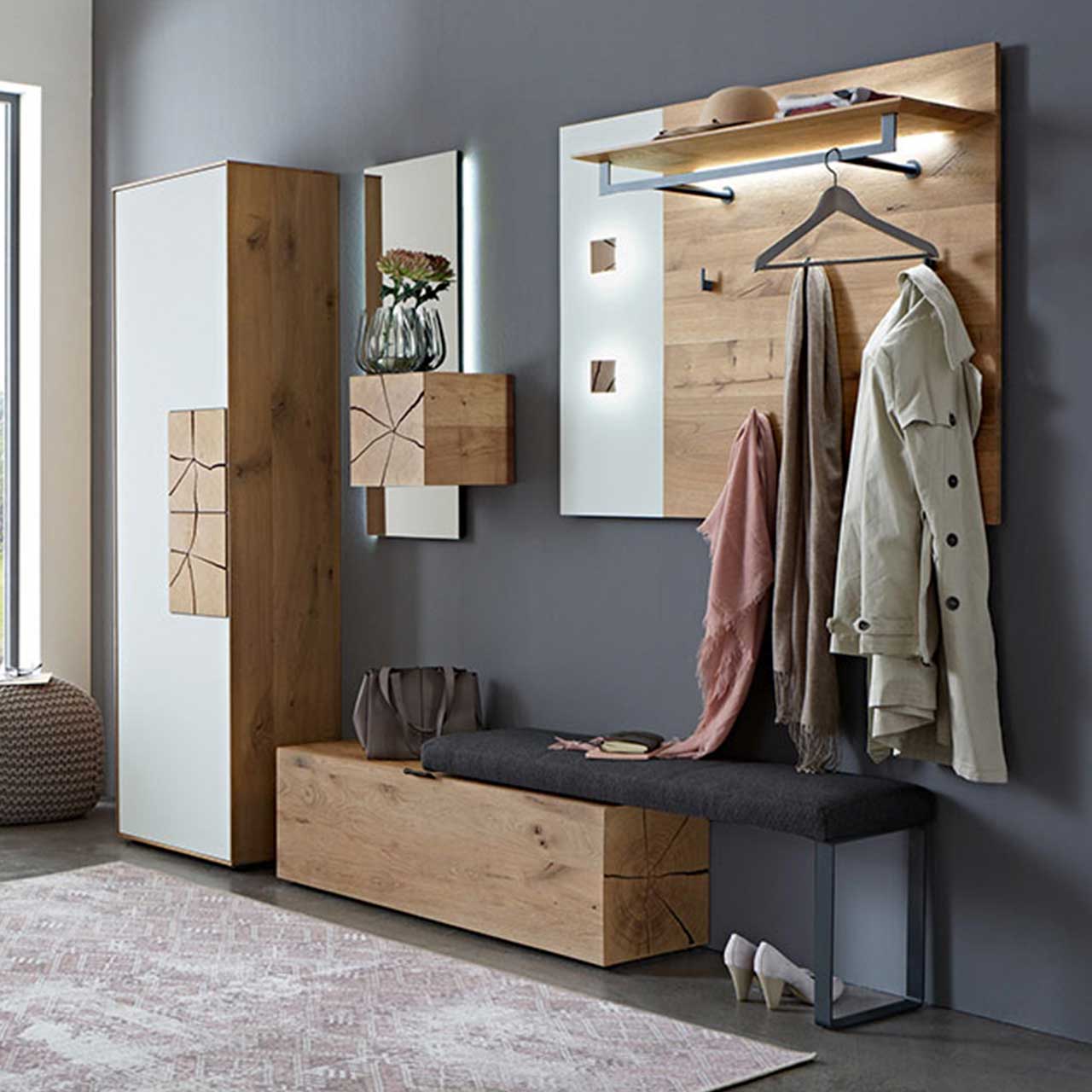 Modern eingerichteter Flur mit Möbeln aus massiver Kerneiche - ein Garderobenpaneel mit Kleidertange und Haken, Hochschrank mit weißen Mattglasfronten und Hirnholz, Polstersitzbank mit Holzfach und einem Spiegel mit aufgesetztem Stauraumfach aus Holz.