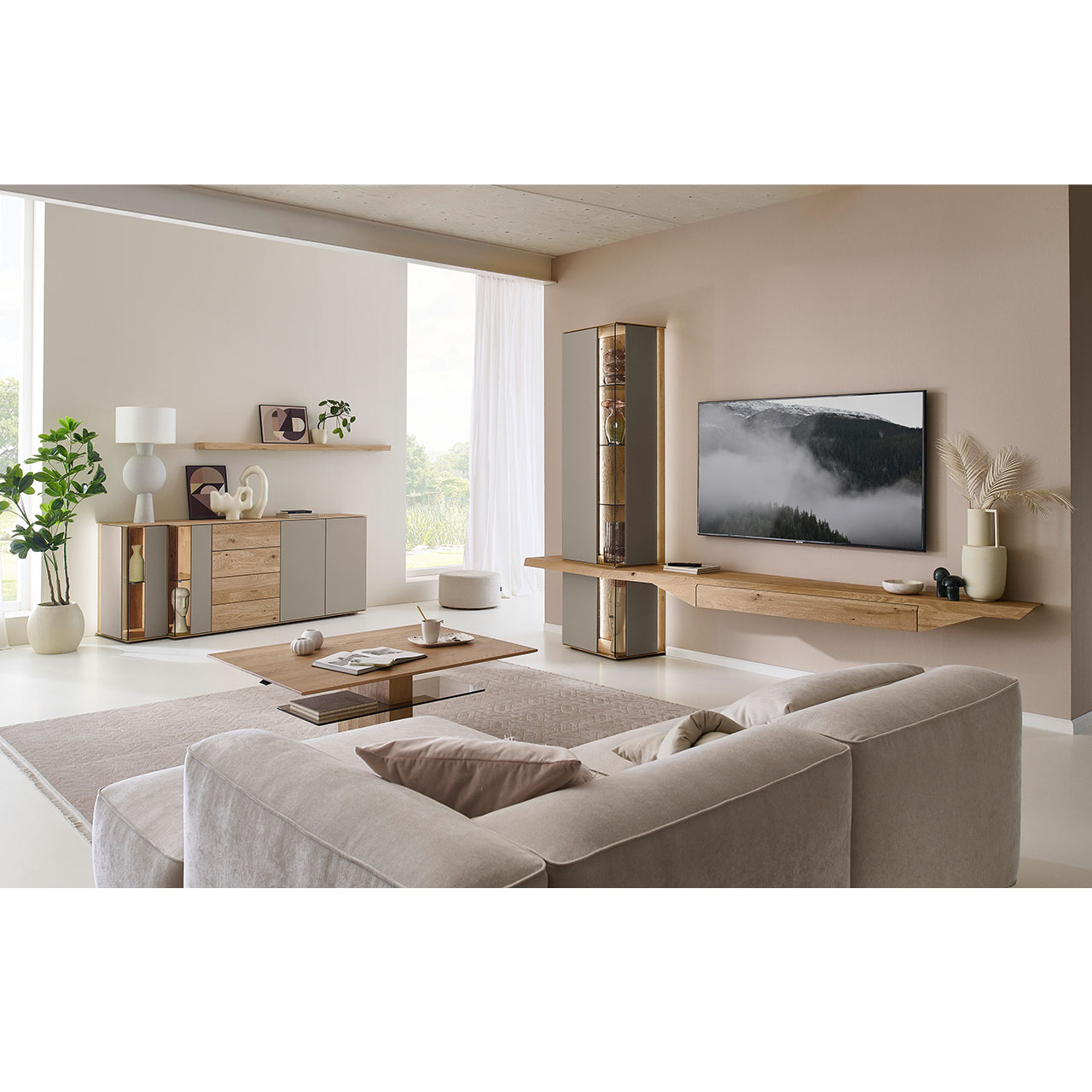 Hartmann Möbel SVEA - Wohnkombination 8660 Nr. V22 - dreiteilig aus Kerneiche Natur, Lack Sand - Milieubild Wohnzimmer mit Massivholzwohnwand aus Kerneiche mit Lack Sand und Riffholz bestehend aus Hängelowboard mit Schubkasten, Hängevitrine sowie Unterbauvitrine - im asymmetrischen Design. Links passendes Sideboard mit Glastüren, davor Holz-Couchtisch.