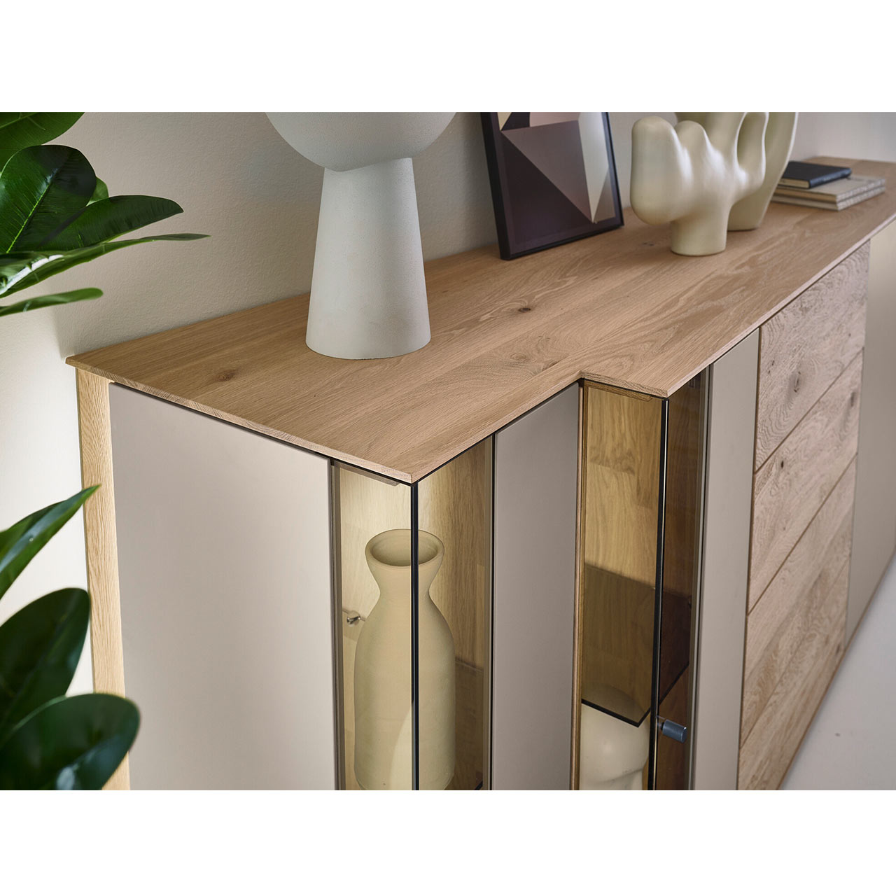 Hartmann Möbel SVEA - Sideboard 8660-4202 - Kerneiche Natur, Lack Sand - Detailansicht Asymmetrisches Design Detailansicht des modernen Sideboards SVEA Nr. 4202 aus massiver Kerneiche Natur und Lack Sand mit asymmetrischer Front aus Glas- und Holzelementen sowie dekorierter Ablagefläche.