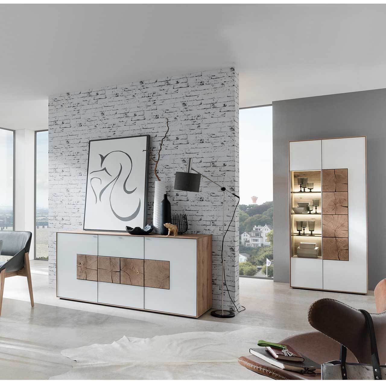 Flur mit modernem Sideboard aus massivem Holz mit Mattglas weiß Front und vier Hirnholzscheiben. Im Hintergrund an einer Wand stehend eine Strandvitrine in Mattglas weiß und beleuchtetem Glasausschnitt mit drei Glasböden.