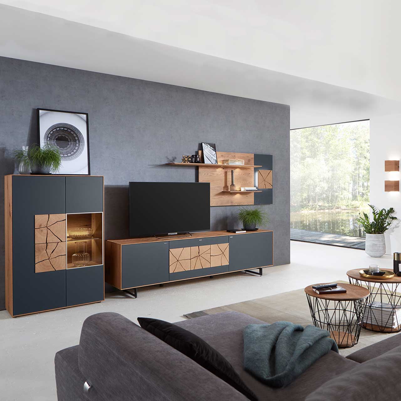 Wohnzimmer mit moderner dreiteiliger Massivholz Wohnwand mit Mattglas Anthrazit Fronten und dekorativen Hirnholzscheiben: Langes Lowboard mit Hirnholz und Kufen, Wandpaneel mit Regalböden, Highboard mit beleuchtetem Glasausschnitt und Hirnholz.