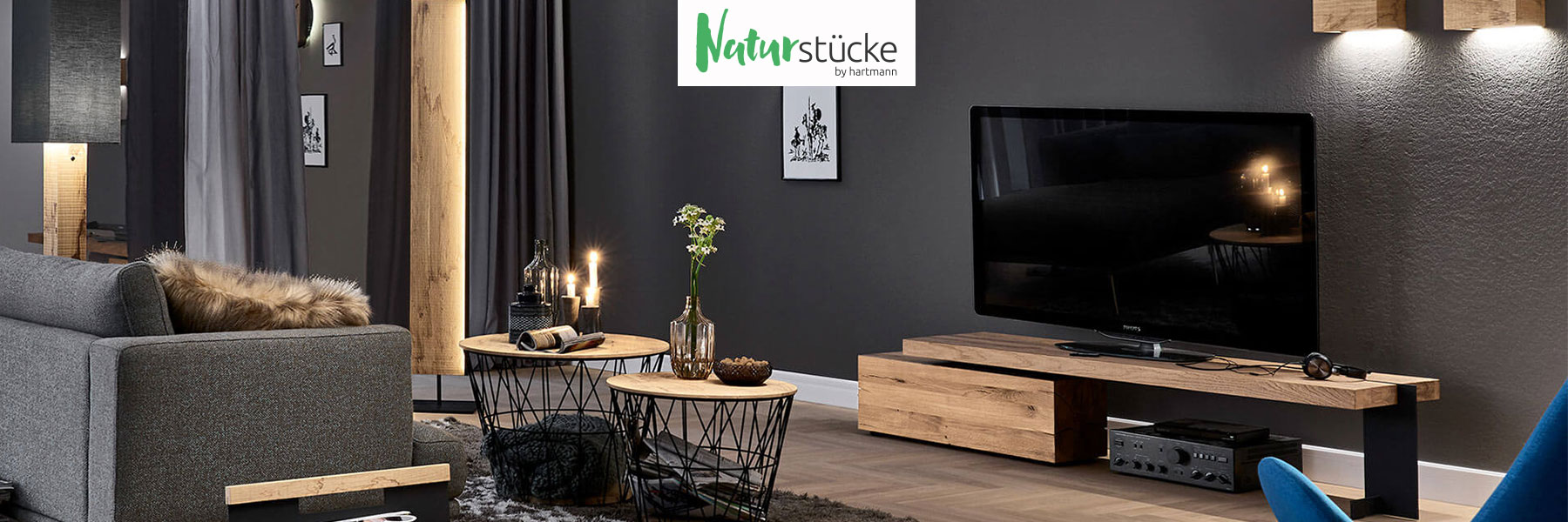 Hartmann NATURSTÜCKE - extravagante Wohnaccessoires aus massiver Birke, Esche oder Kerneiche kombiniert mit Glas und Metall. Ambientebild zeigt verschiedene Stehlampen, Zeitungsständer, Wandleuchten, Beistelltische aus hochwertigem Holz.