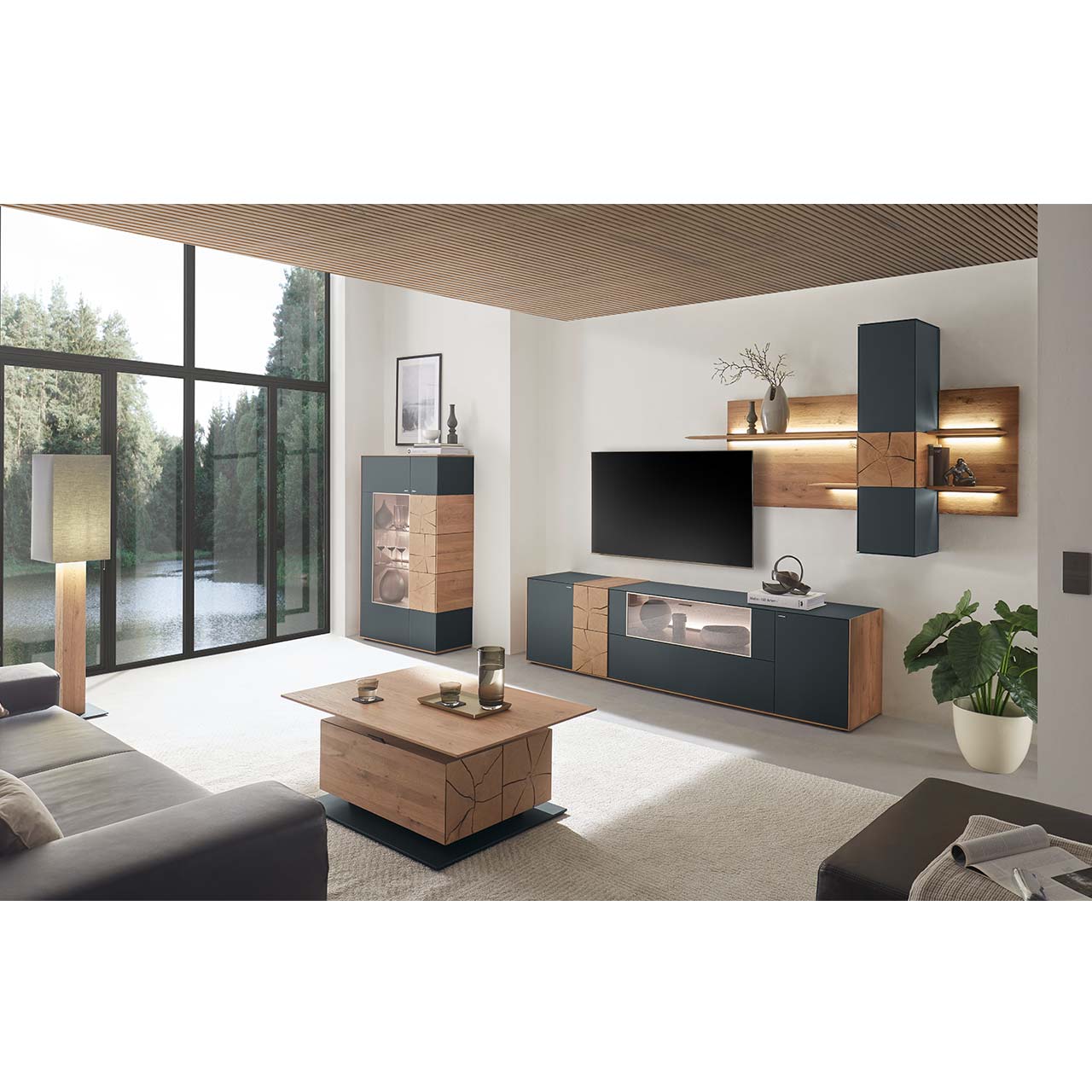 Moderne Wohnwand aus massiver Kerneiche mit anthrazitfarbenen Fronten, mit Lowboard mit Glasausschnitt sowie Wandpaneel mit Regalböden und Hängeschrank. Links ein Highboard mit Glasfront und Hirnholzscheiben. Im Vordergrund der passende Couchtisch. 