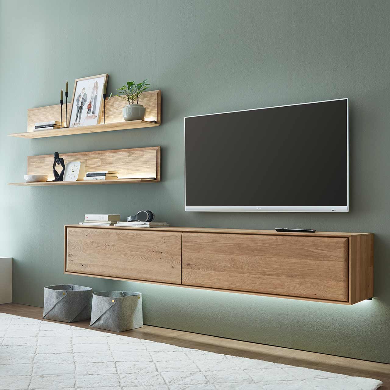 Moderne dreiteilige Wohnwand aus massiver Kerneiche Natur bestehend aus einem Hängelowboard mit zwei Klappen sowie zwei beleuchteten Wandpaneelen mit Holzboden und geschroppter Rückwand. Hartmann VALA - Wohnkom