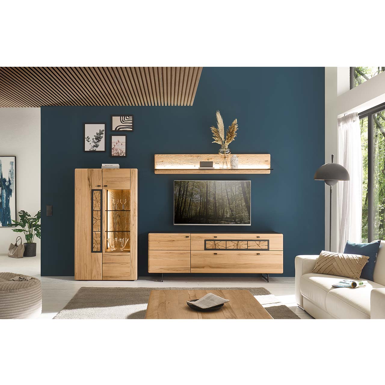 Wohnzimmer mit Fernseher und Massivholzwohnwand in Kernbuche bestehend aus Highboard mit Glasfront, langes Lowboard auf Metallkufen mit Holztür und Schubkästen mit Hirnholzscheiben darüber hängt das passende lange Wandpaneel mit Glasablage.