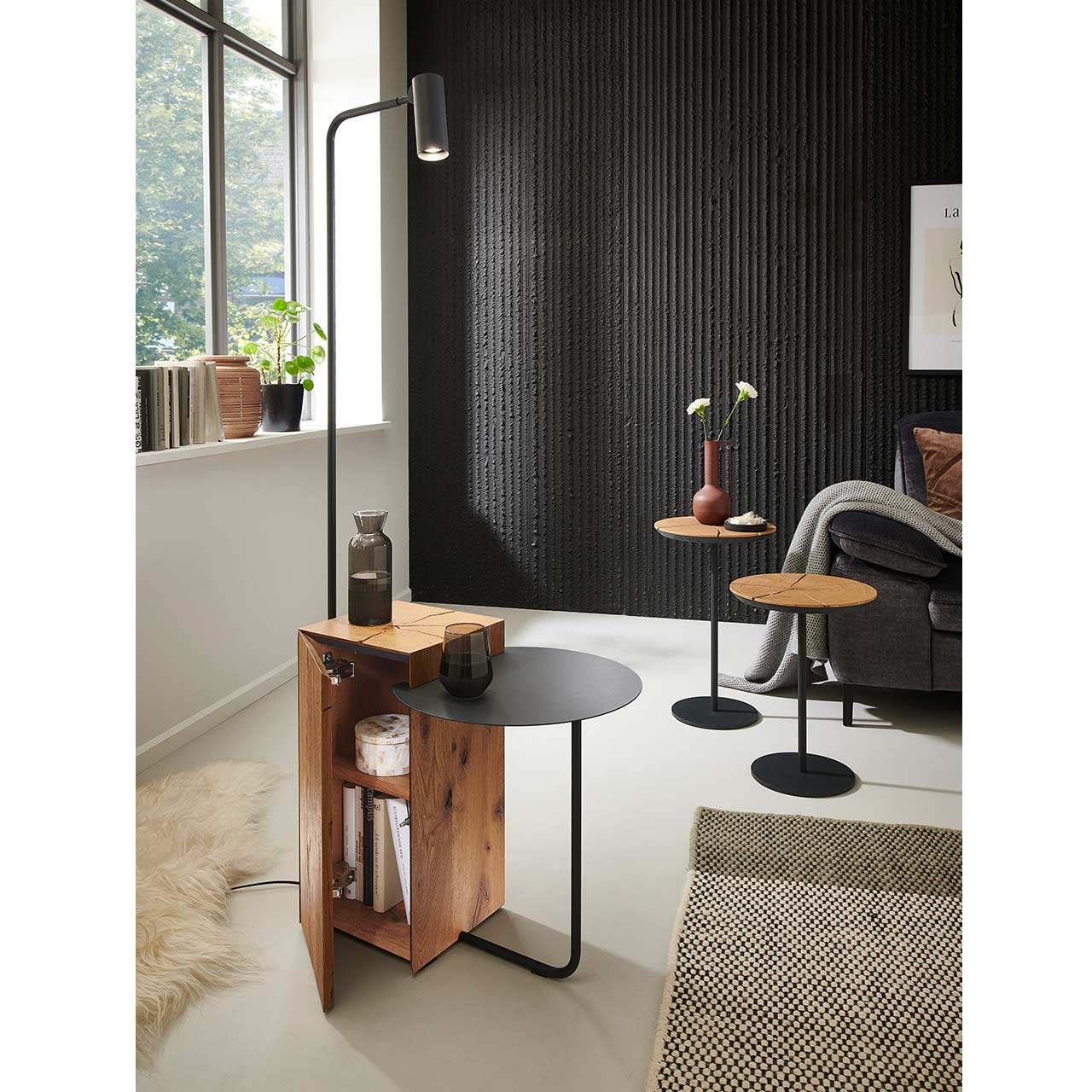 Modernes Wohnzimmer mit zwei runden Beistelltischen aus Kerneiche und Metall, daneben kleiner Tisch mit Leselampe und offenem Holzschrank mit Fächern.