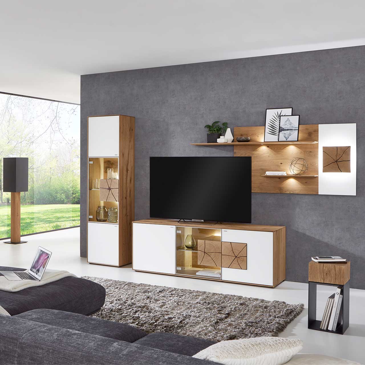 Wohnzimmer mit moderner dreiteiliger Massivholz Wohnwand mit Mattglas weiß Fronten und Hirnholzscheiben: Lowboard mit Glastür und beleuchtetem Hirnholzblock, Wandpaneel mit Regalböden, Standvitrine mit beleuchtetem Glasausschnitt und Hirnholz.