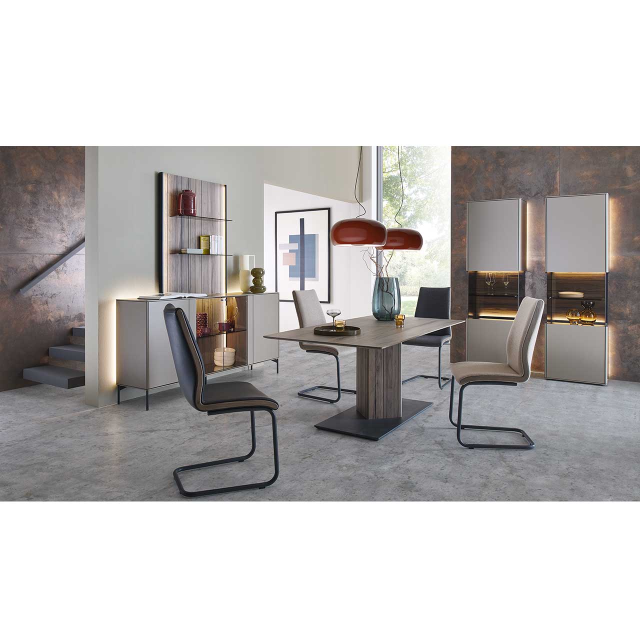 Modern eingerichtetes Esszimmer mit rechteckigem Tisch aus massiver Altholzbuche Uyaa und vier Freischwingern mit hellem Lederbezug. Rechts an der Wand zwei beleuchtete Standvitrinen mit  sandfarbenen Lackfronten. Links das passende Sideboard mit Paneel.