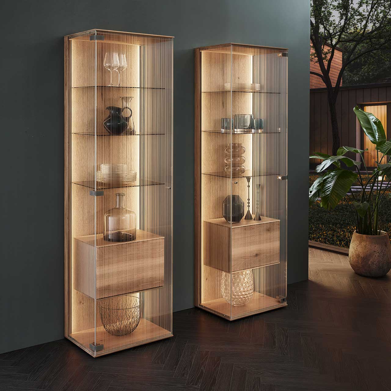 Zwei moderne Standvitrinen aus Kerneiche Natur mit satiniertem Glas auf drei Seiten und innenliegendem Holzkorpus mit Klappe – platziert vor einer dunklen Wand