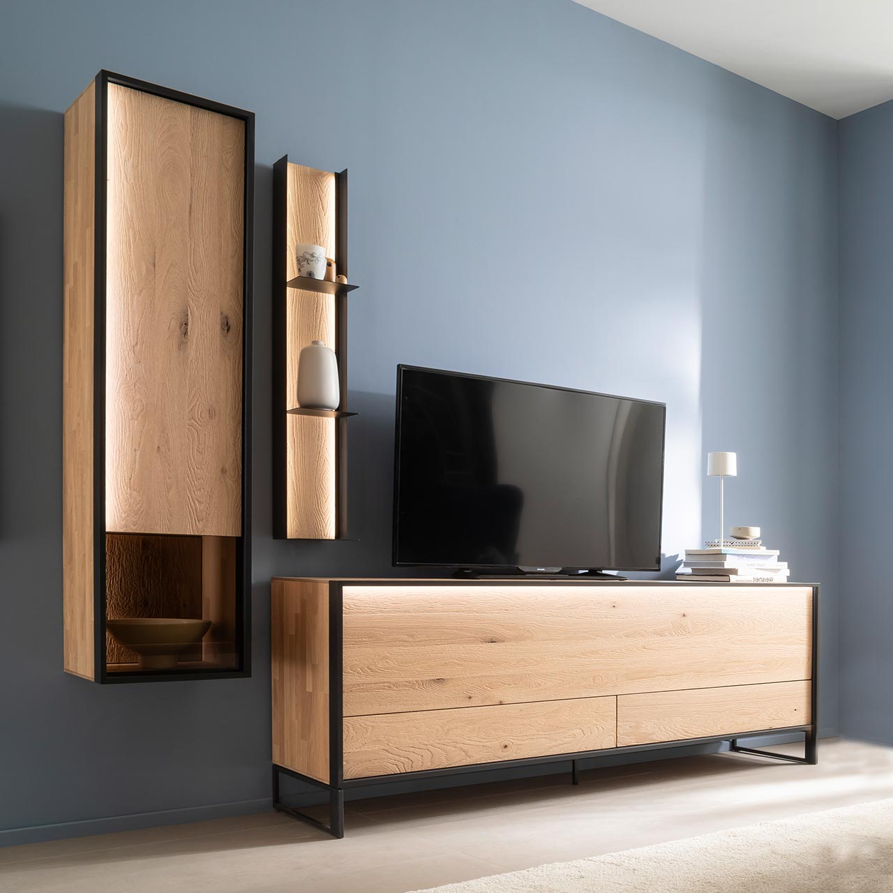 Hartmann YOLA Schöner Wohnen - Wohnkombination 8590 Nr. V22SV Moderne dreiteilige Wohnwand aus massiver sandgestrahlter Kerneiche Natur, Möbelstücke eingefasst in Metall anthrazit: Schlichtes Lowboard auf Metallkufen, Hängeschrank mit beleuchtetem Glasausschnitt, Regal mit drei Metallablagen.