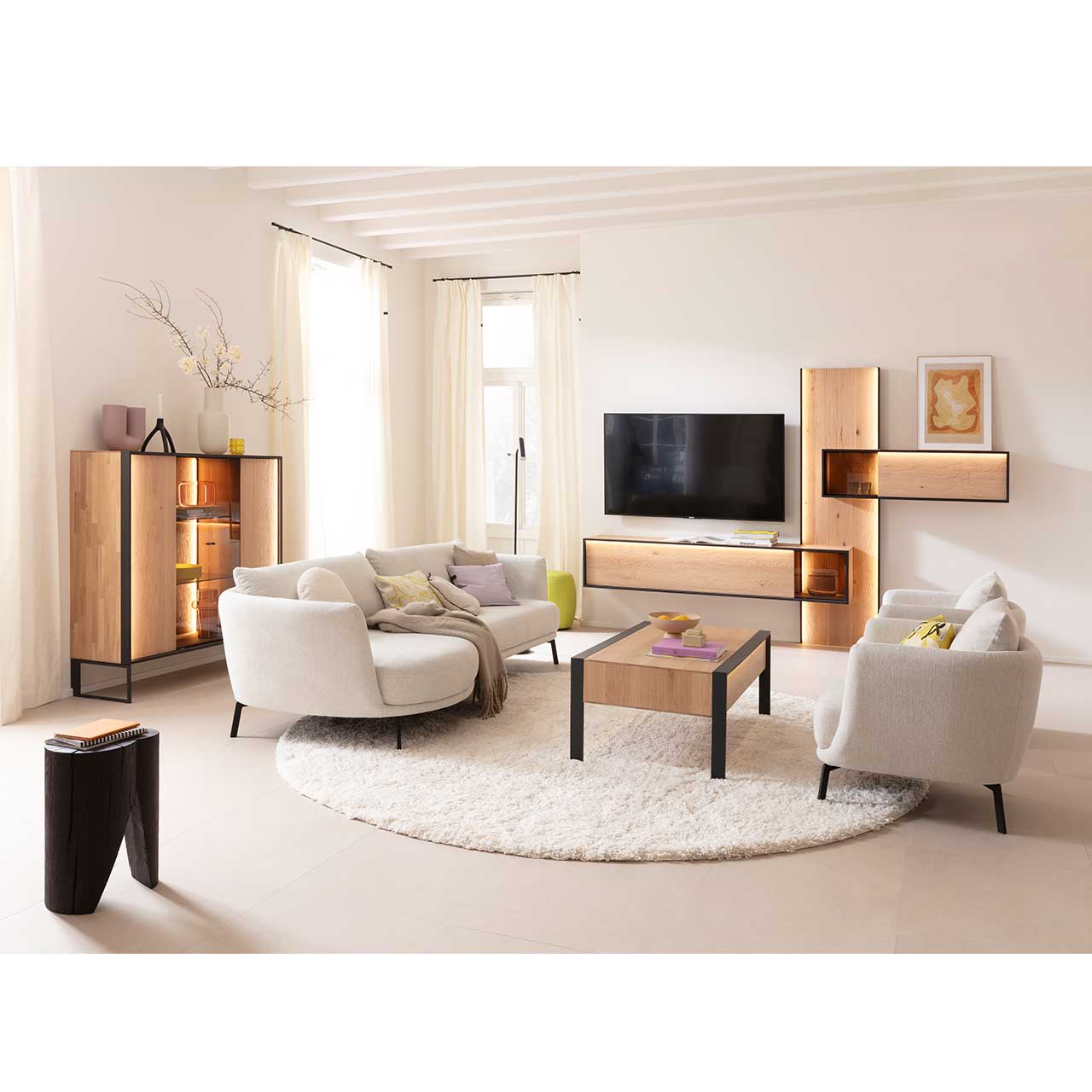 Wohnzimmer mit Wohnwand aus sandgestrahlter Kerneiche Natur mit anthrazitfarbenem Metallrahmen, Hängeregal mit Glasausschnitt, Hängelowboard mit Glasdetail, kombiniert am langen Wandpaneel, links passendes Highboard, davor Holz-Couchtisch.