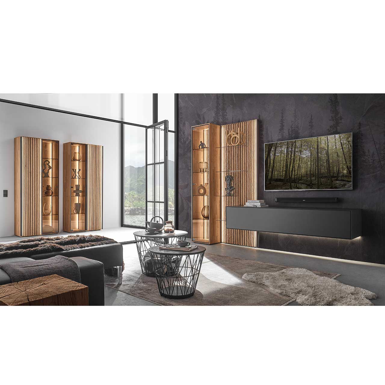 Modernes Wohnzimmer mit dreiteiliger Wohnwand aus dunkler Birke und heller Kerneiche mit Holzlamellen: Hängelowboard, Vitrine und Wandpaneel. Links an der Wand zwei passende Standvitrinen in hellem Holz und Lamellen.