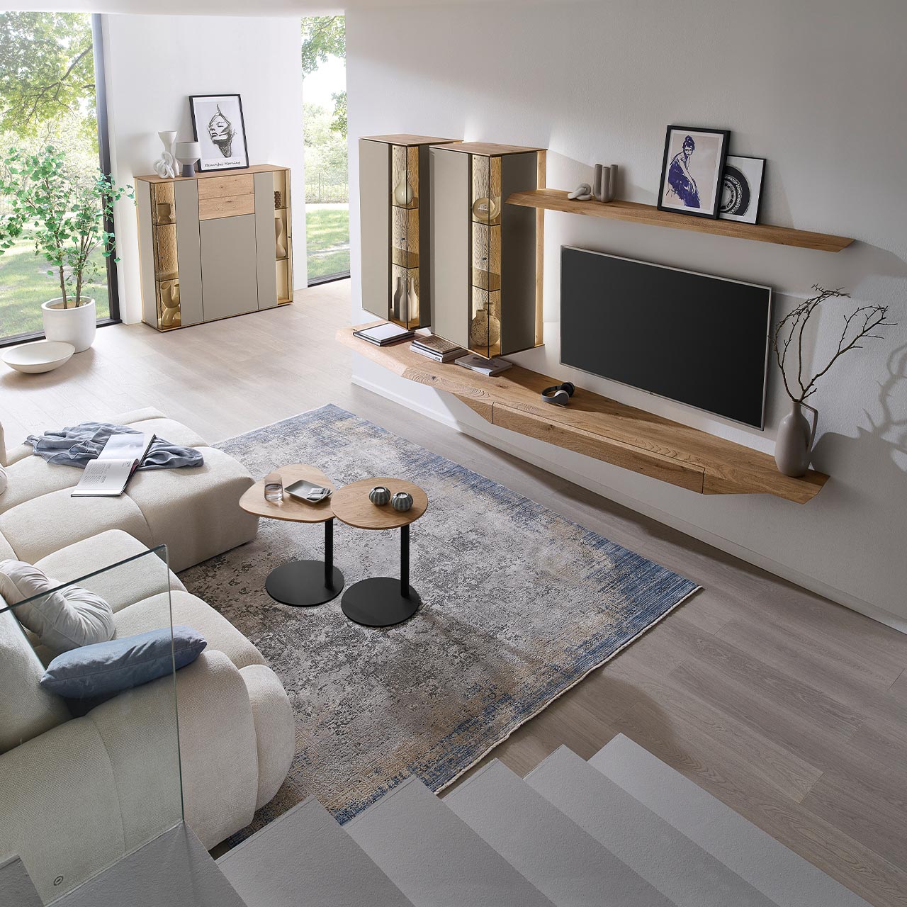 Wohnzimmer mit moderner Massivholzwohnwand bestehend aus Hängelowboard, Hängevitrinen, sowie Wandboard - im asymmetrischen Design. Links passendes Highboard mit Glastüren, davor zwei Beistelltische aus Holz - Ansicht von oben.