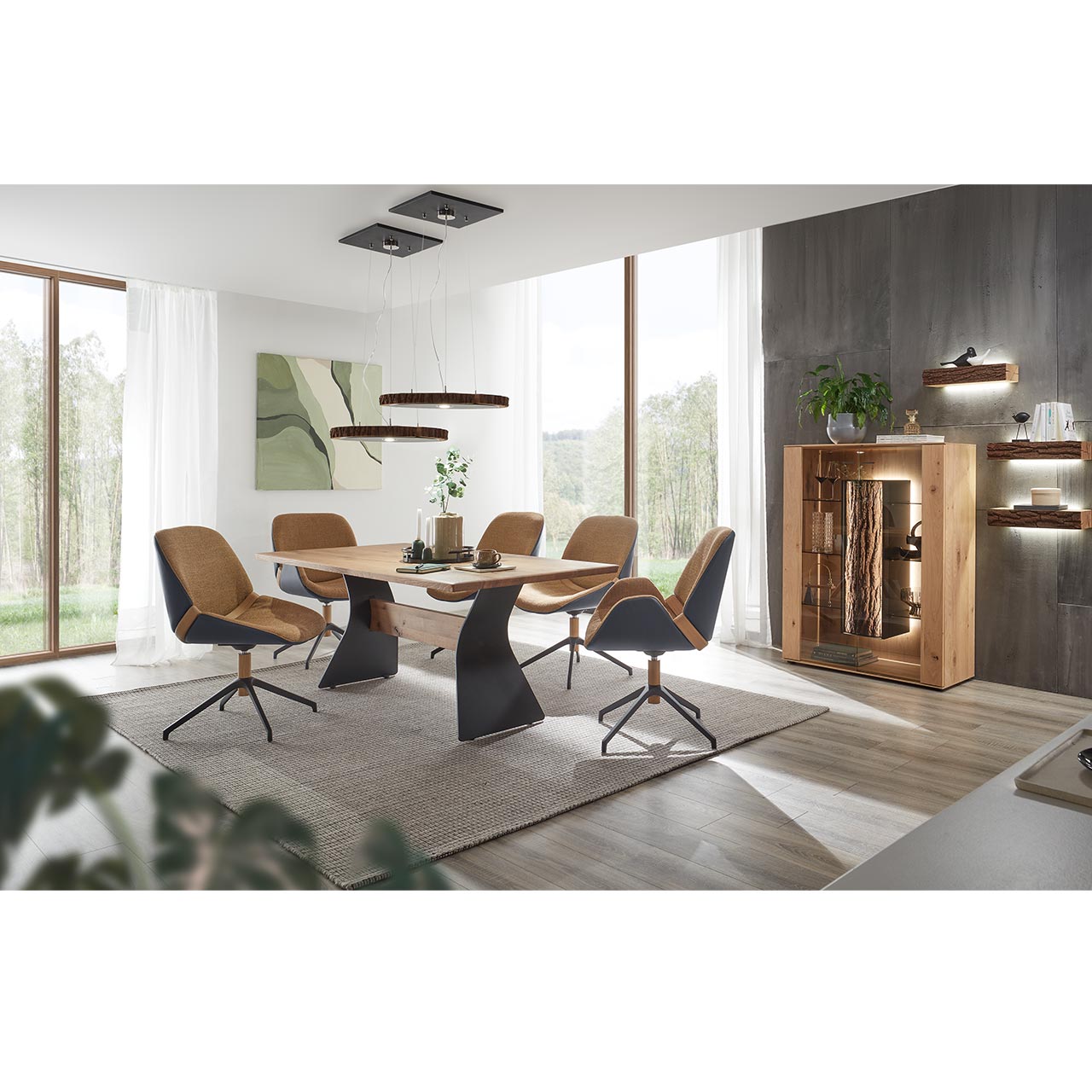 Modern eingerichtetes Esszimmer mit Esstisch aus hellem Holz mit geschwungenem 2-Fuß-Metallgestell Anthrazit und mittig liegendem Holztravers. Umgeben von fünf modernen Stühlen in beigem Stoff, mit Außensitzschale und Metallgestell anthrazit.