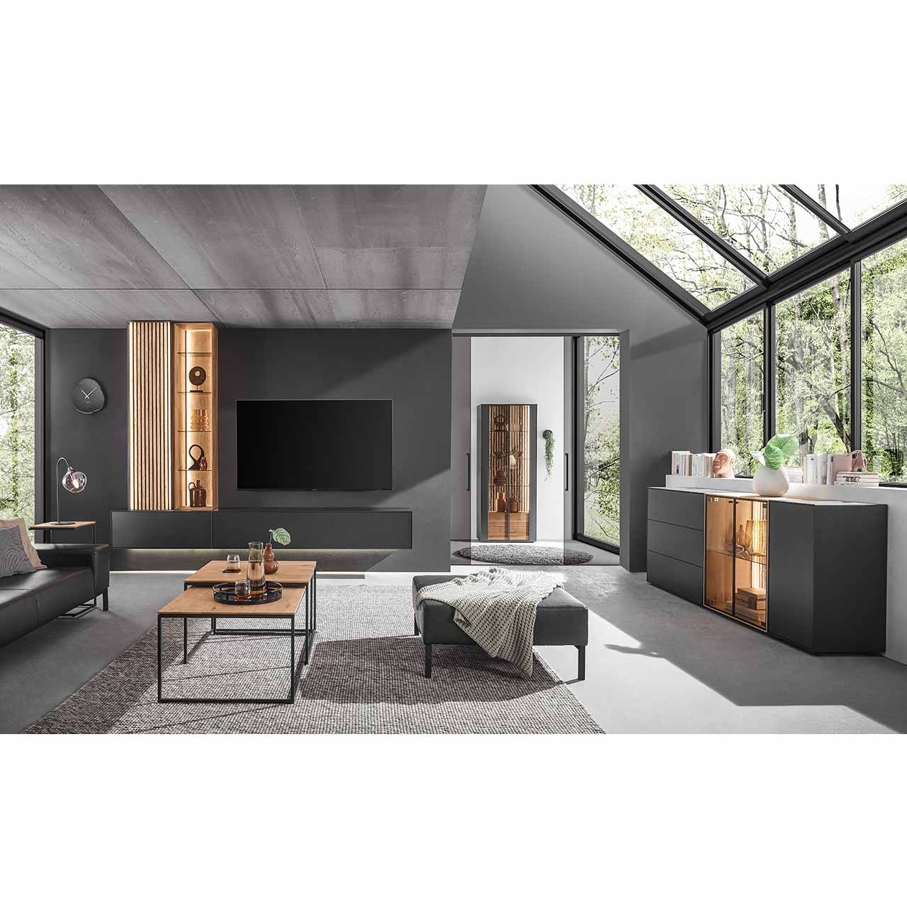 Modern eingerichtetes Wohnzimmer mit vierteiliger Wohnwand in Anthrazit kombiniert mit hellem Holz und Lamellen. Mit passendem Sideboard rechts und minimalistischem Couchtisch im Vordergrund.