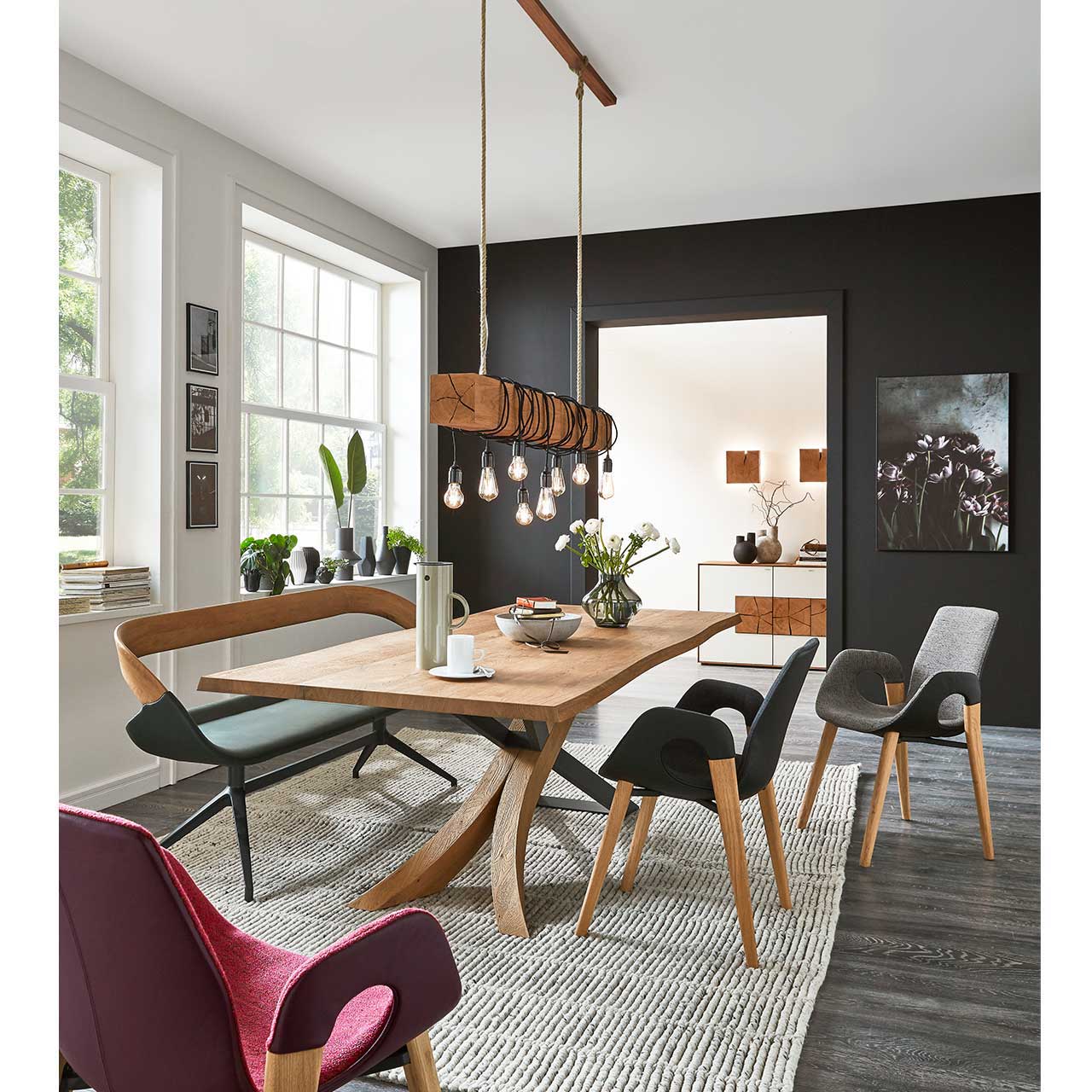 Modernes Esszimmer mit rechteckigem Holztisch, Stühlen mit Holzgestell und der passenden Polstersitzbank. Darüber hängend eine Balkenleuchte aus Holz. 