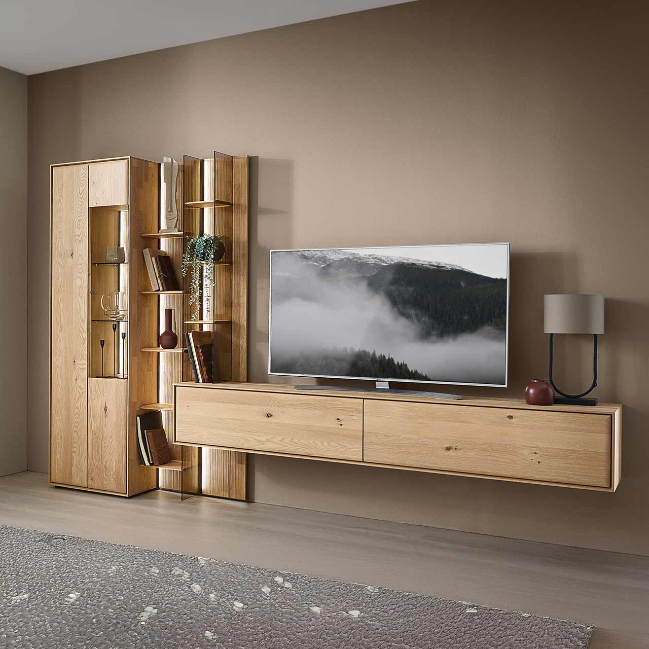 Moderne dreiteilige Wohnwand aus massiver Kerneiche Natur bestehend aus einer Standvitrine, einem hohen Wandregal mit Holzböden, beleuchteten Glasseiten und geschroppter Rückwand und einem darin integriertem Hängelowboard