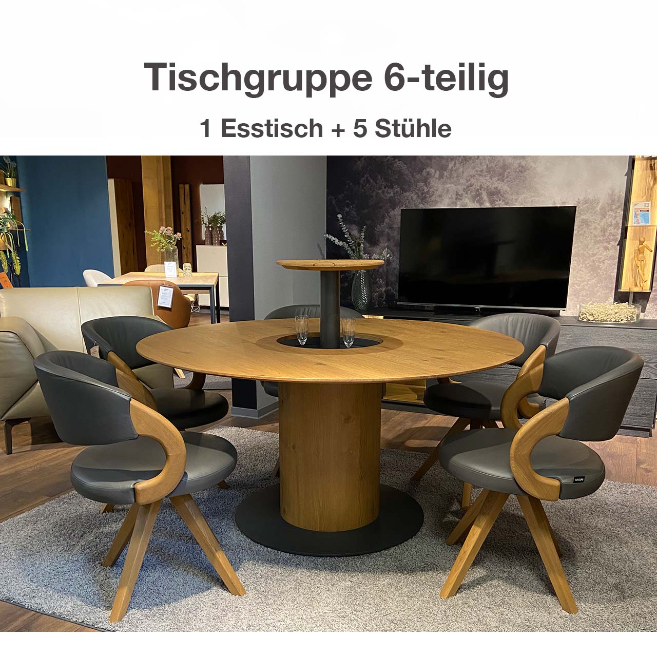 Moderne Esstischgruppe aus massiver Kerneiche Umato, bestehend aus einem runden Esstisch mit mittigem, offenem Flaschenfach in der Tischplatte. Um den Tisch stehen fünf drehbare Stühle mit Holzlehne und Holzgestell, bezogen mit grauem Leder.