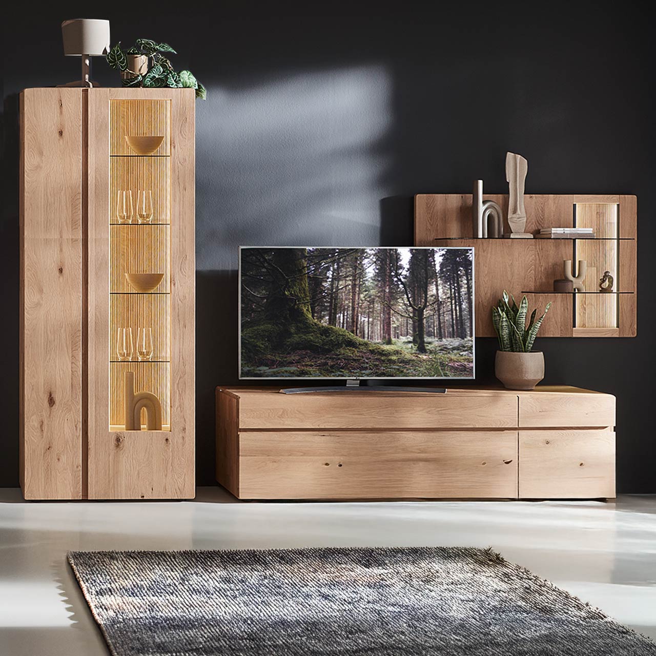 Moderne dreiteilige Wohnwand aus massiver Kerneiche Natur bestehend aus Lowboard mit Tür und Schubkasten, rechts Wandpaneel mit zwei Glasböden sowie beleuchteter, geschroppter Rückwand, links beleuchtete Standvitrine mit Holz-/Glastüren.