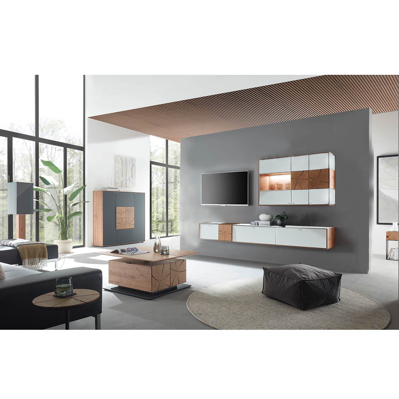 Wohnzimmer mit TV und moderner Wohnwand aus massiver Kerneiche und Mattglas weiß Fronten, mit schmalem Hängelowboard und beleuchteter Hängevitrine. Links das passende Highboard. Im Vordergrund ein rechteckiger Holz-Couchtisch.