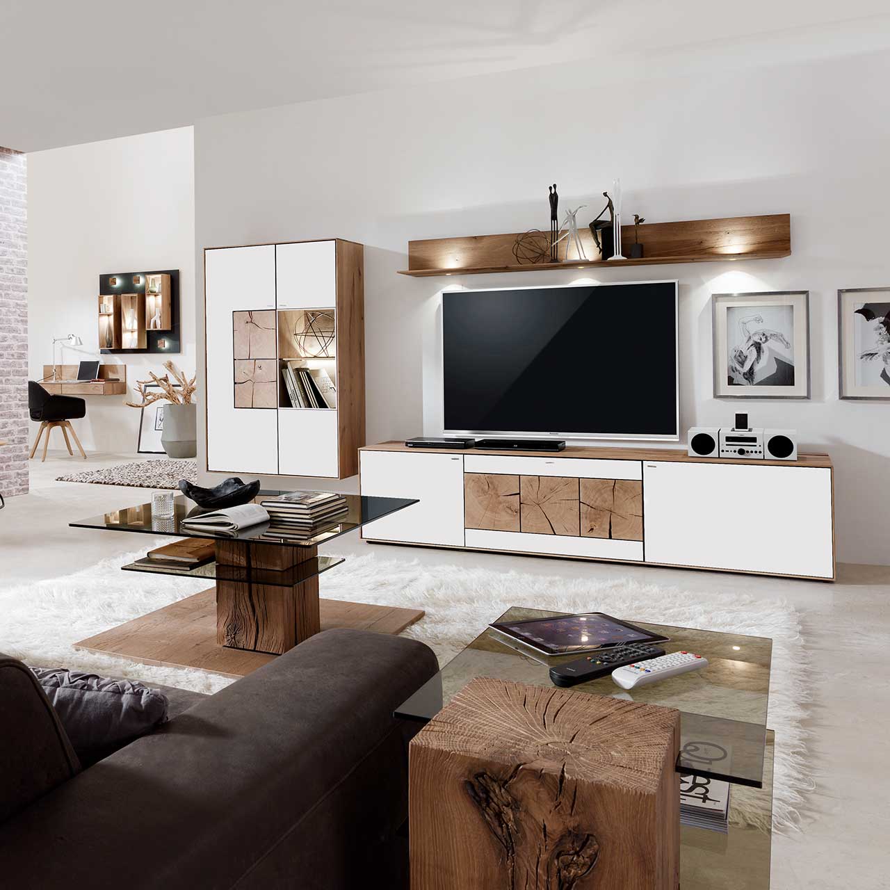 Milieubild Hartmann CAYA - Hängeelement 7170-7095W li. Wohnzimmer mit moderner dreiteiliger Massivholz Wohnwand mit Mattglas weiß Fronten und dekorativen Hirnholzscheiben: Lowboard mit Hirnholz, Wandregal mit Spotbeleuchtung, große Hängevitrine mit beleuchtetem Glasausschnitt und Hirnholz.
