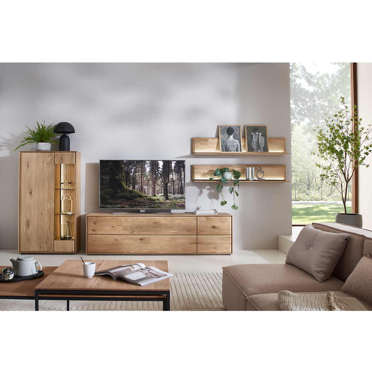 Wohnzimmer mit moderner Massivholzwohnwand bestehend aus aus einem Lowboard mit Schubkästen, einem Highboard mit Glastür sowie zwei beleuchteten Wandpaneelen mit Holzboden und geschroppter Rückwand. Davor passender Couchtisch.