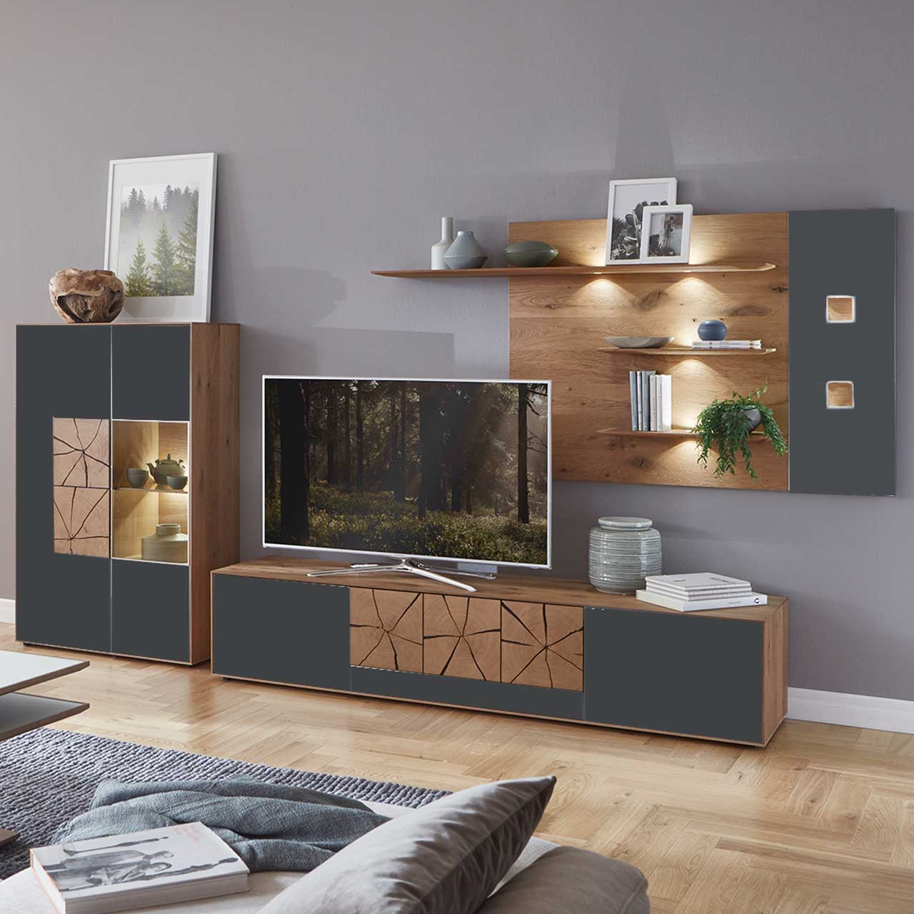 Wohnzimmer mit moderner dreiteiliger Massivholz Wohnwand mit Mattglas Anthrazit Fronten und dekorativen Hirnholzscheiben: Langes Lowboard mit Hirnholz, Wandpaneel mit Regalböden, Highboard mit beleuchtetem Glasausschnitt und Hirnholz.