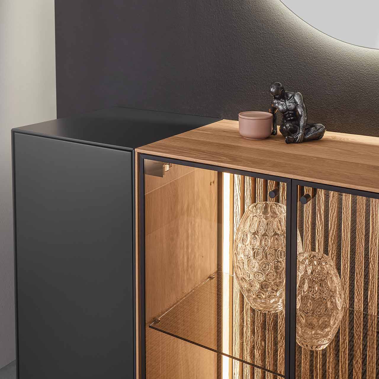 Detailaufnahme der Glastür aus Parsolbronze mit beleuchteter Lamellenrückwand von einem Sideboard aus massiver Birke anthrazit lackiert.